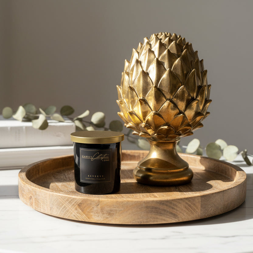 Gold artichoke-shaped ornament and black & gold candle on a wooden surface against a white wall.