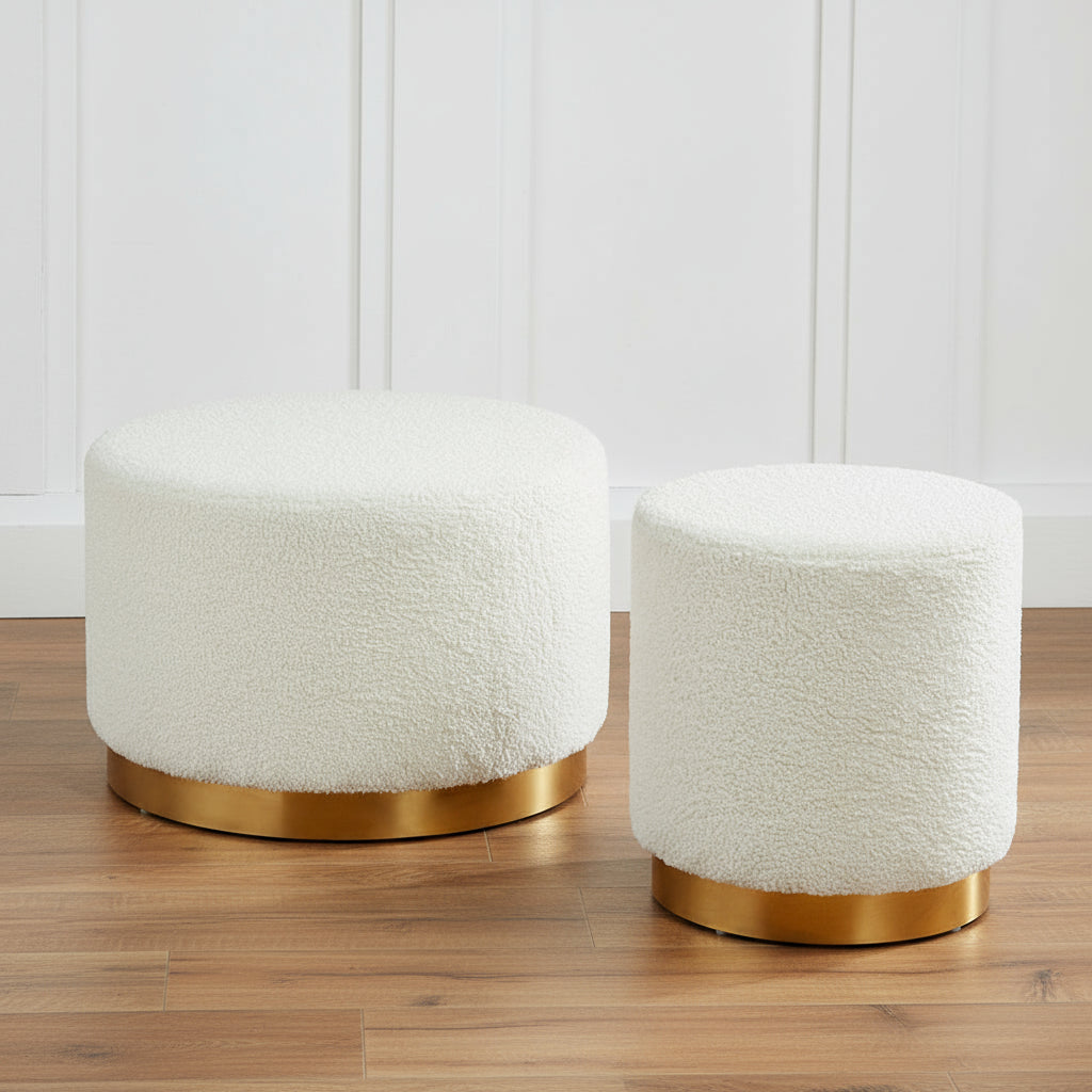 HARRY CHRISTIAN HOME Two white textured stools with gold bases on a gray surface against a dark paneled wall.Harry Christian Home Teddy Bear White Footstool / Pouffe With Brushed Gold Base